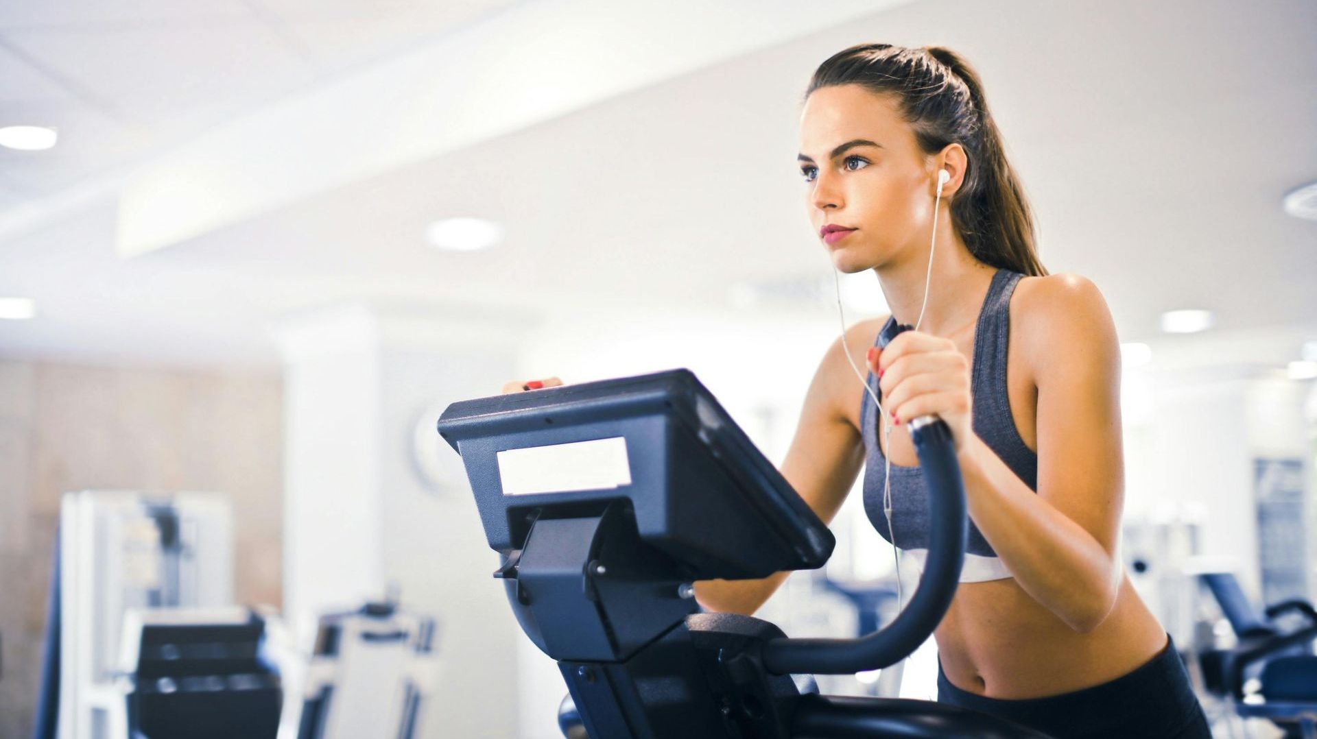 A woman is riding an exercise bike in a gym while listening to music.