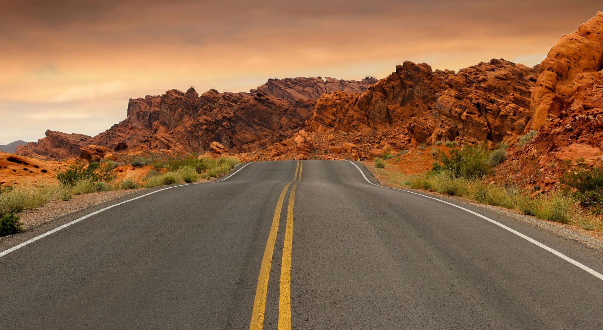 An empty road in the desert with mountains in the background