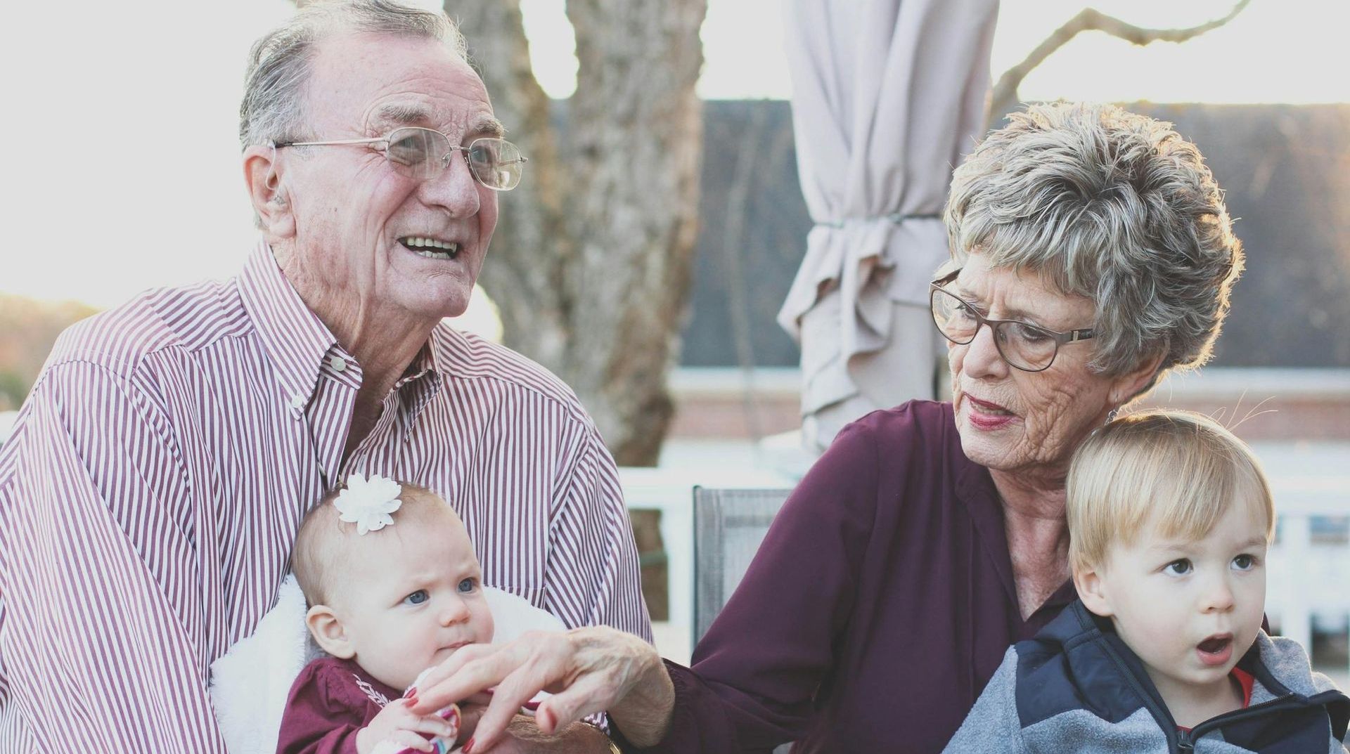 An elderly couple is holding a baby and two children while sitting on a porch.