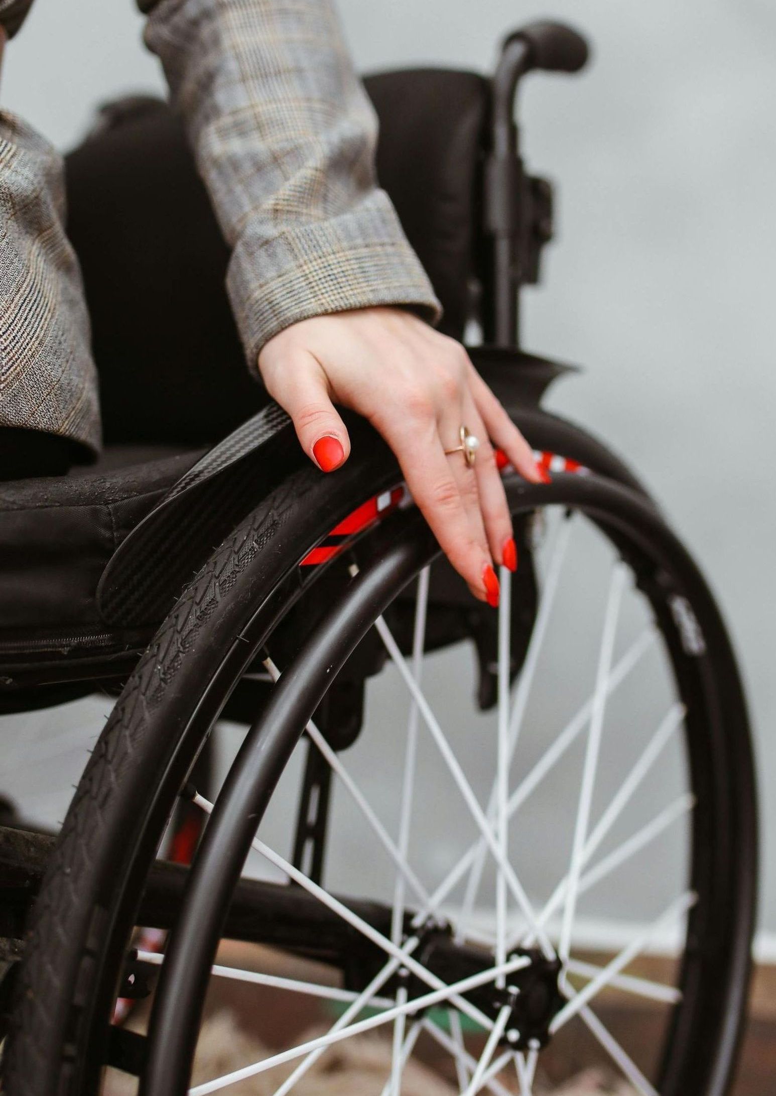 A woman in a wheelchair with red nails and a ring on her finger.