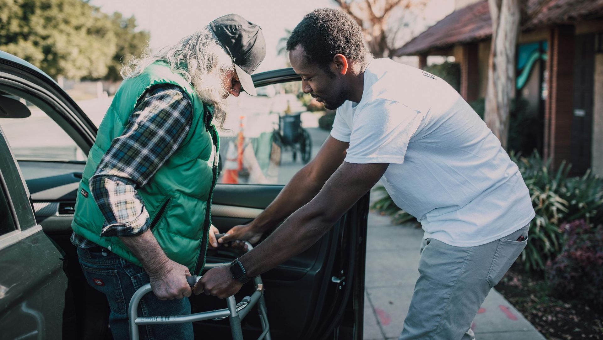 A man is helping an older man with a walker into a car.