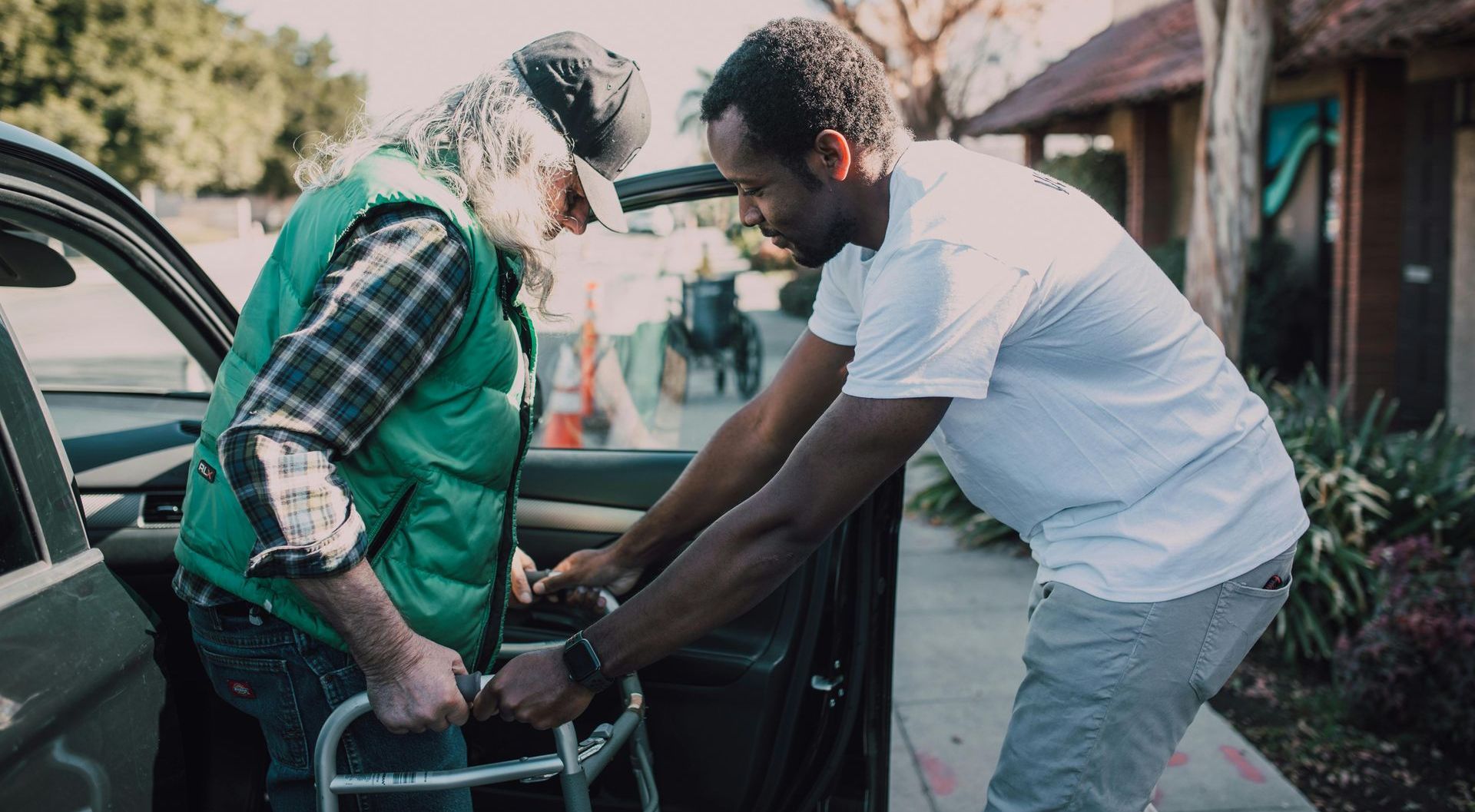 a man is helping an elderly man with a walker into a car.