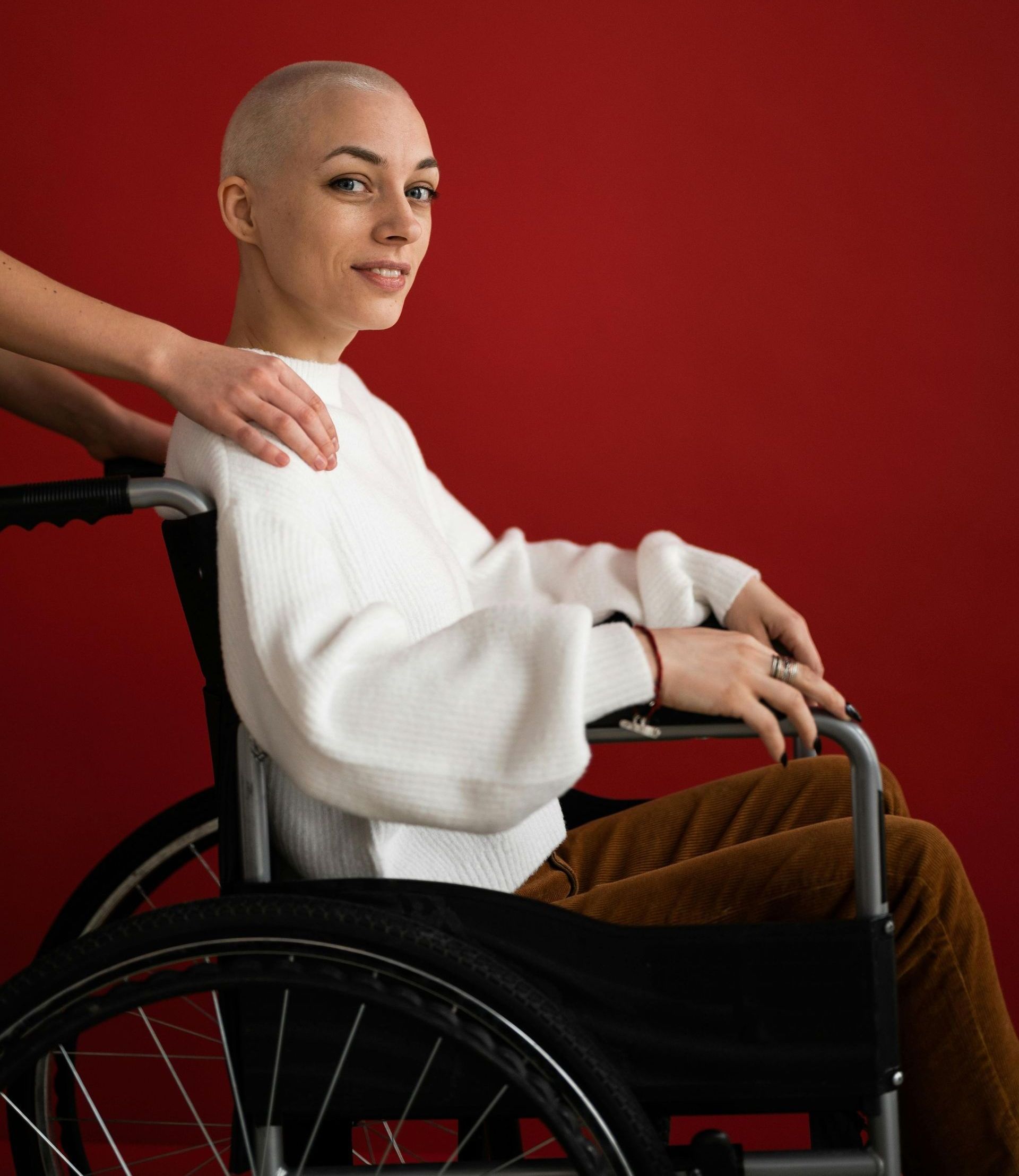 A woman is sitting in a wheelchair with her hand on her shoulder.