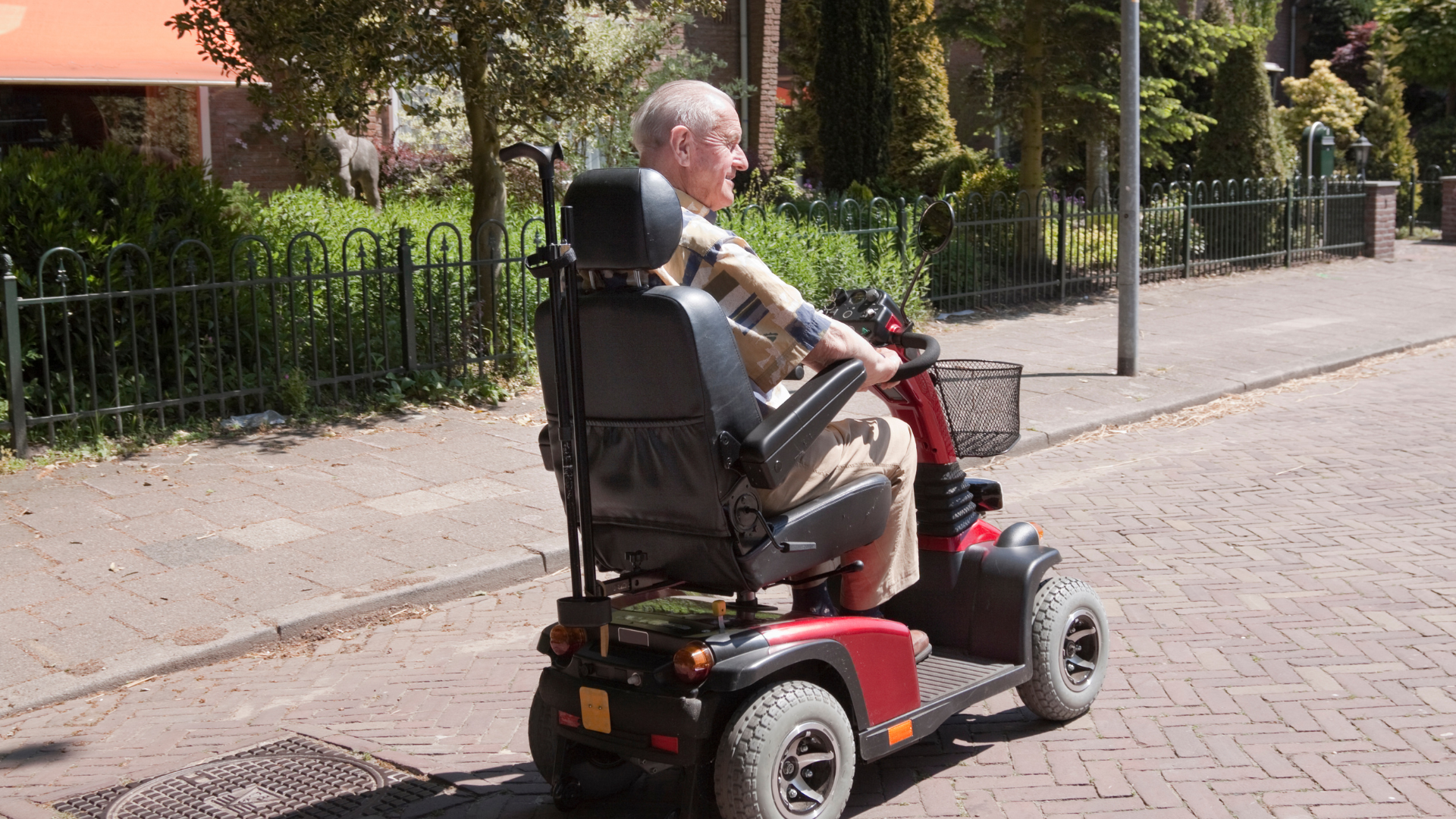 An elderly man is riding a mobility scooter down a brick street.