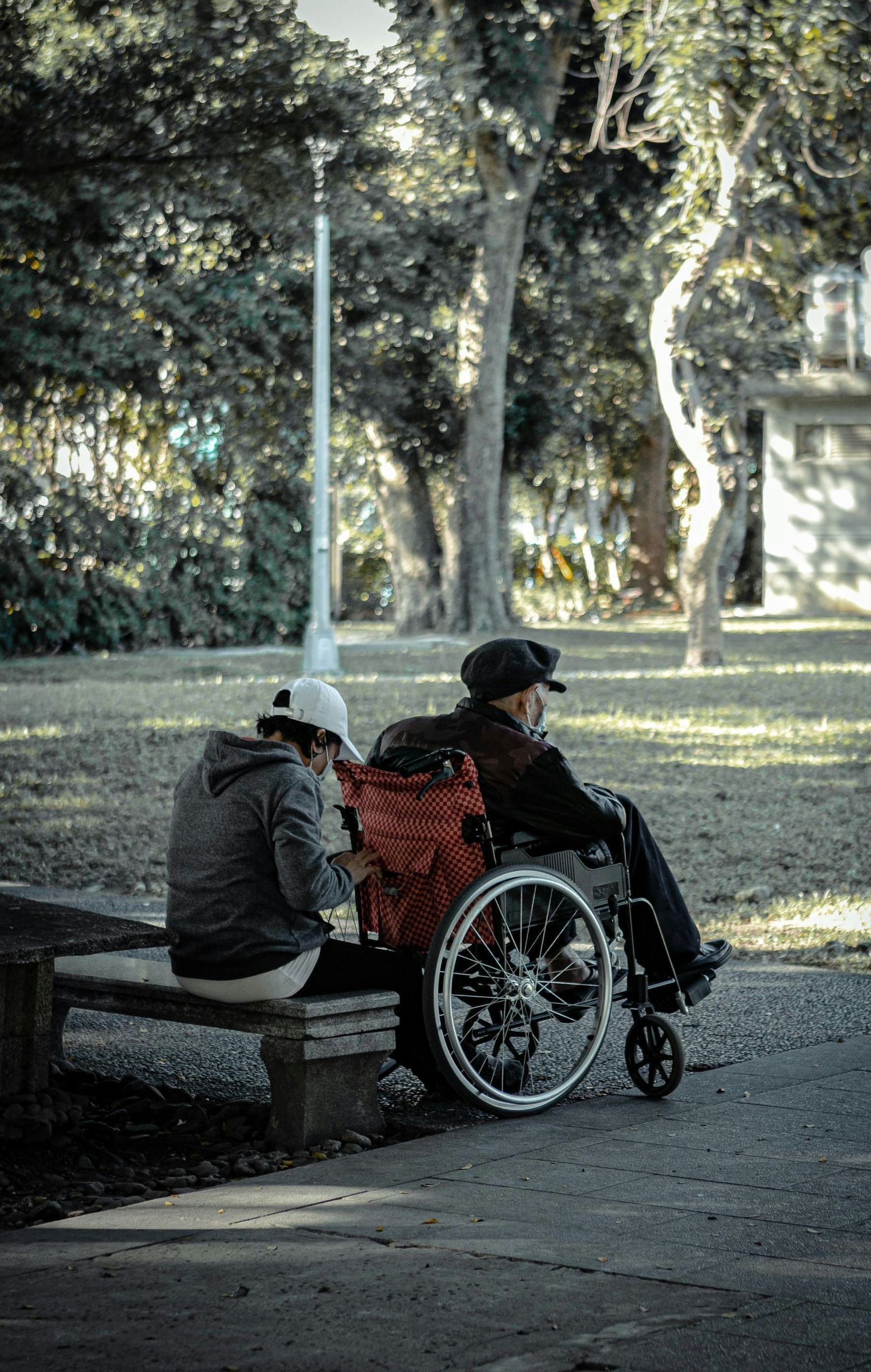 A woman is sitting on a bench next to a man in a wheelchair.
