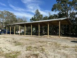 A large wooden structure with a metal roof is sitting in the middle of a dirt field.