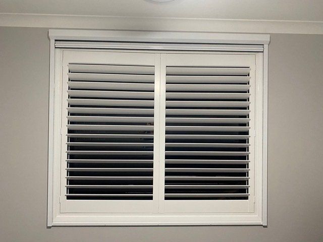 A window with white shutters on it in a room — Plantation Shutters in Singleton, NSW