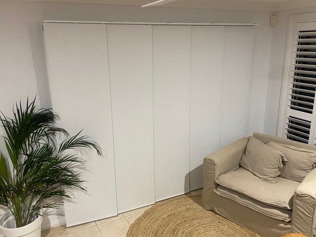 A living room with a couch , chair , and plant — Plantation Shutters in Singleton, NSW