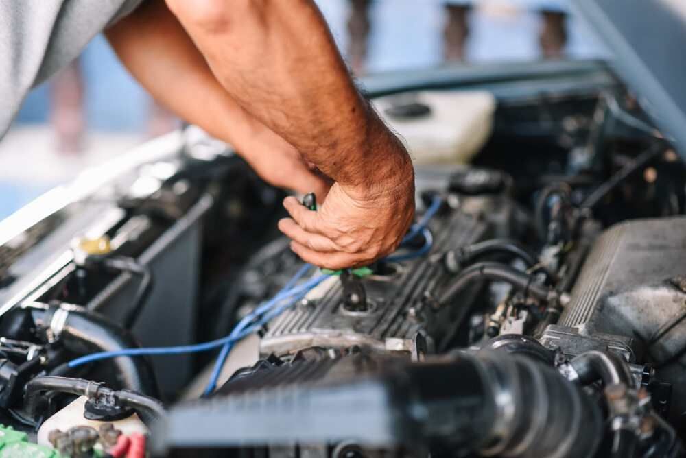 A Man Is Working On The Engine Of A Car With A Screwdriver — Baker Automotive In Bungalow, QLD