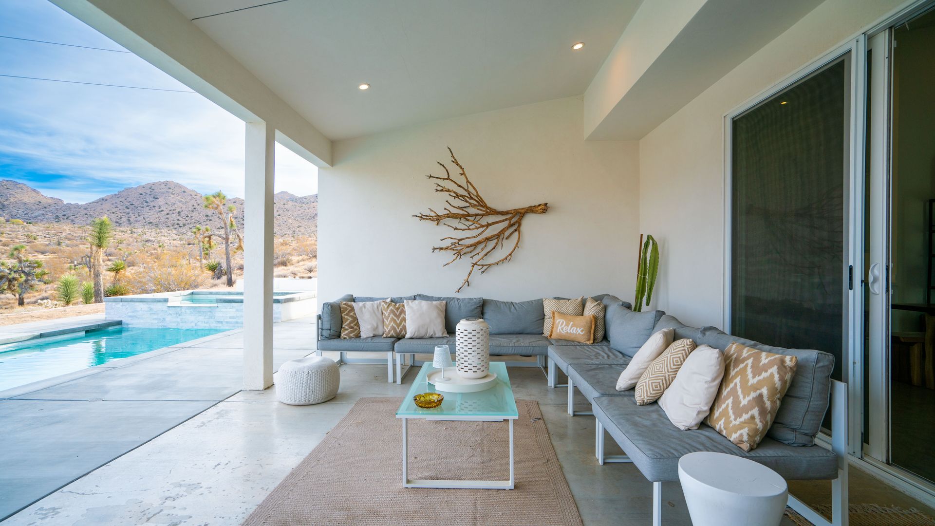 Covered outdoor patio with seating, coffee table, and pool overlooking mountains.