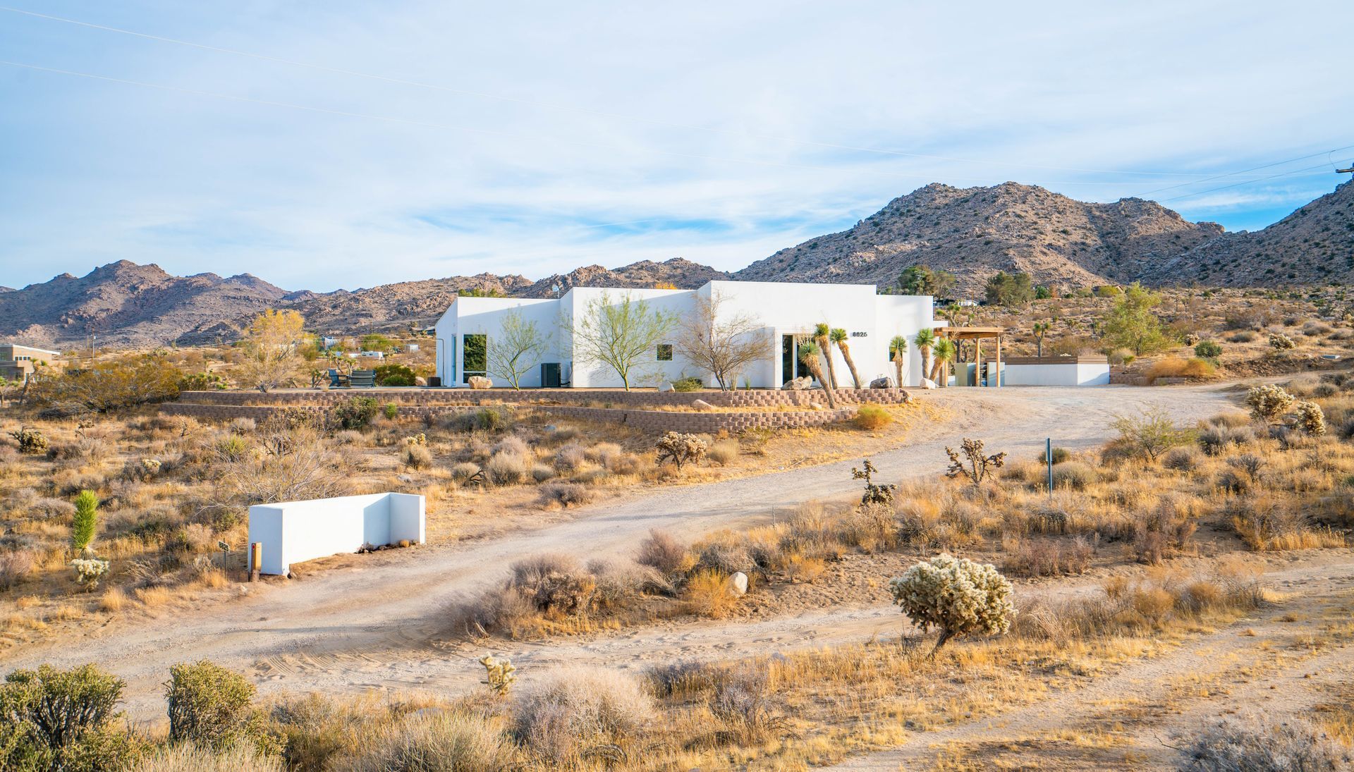 White stucco house in desert landscape with mountains in the background.