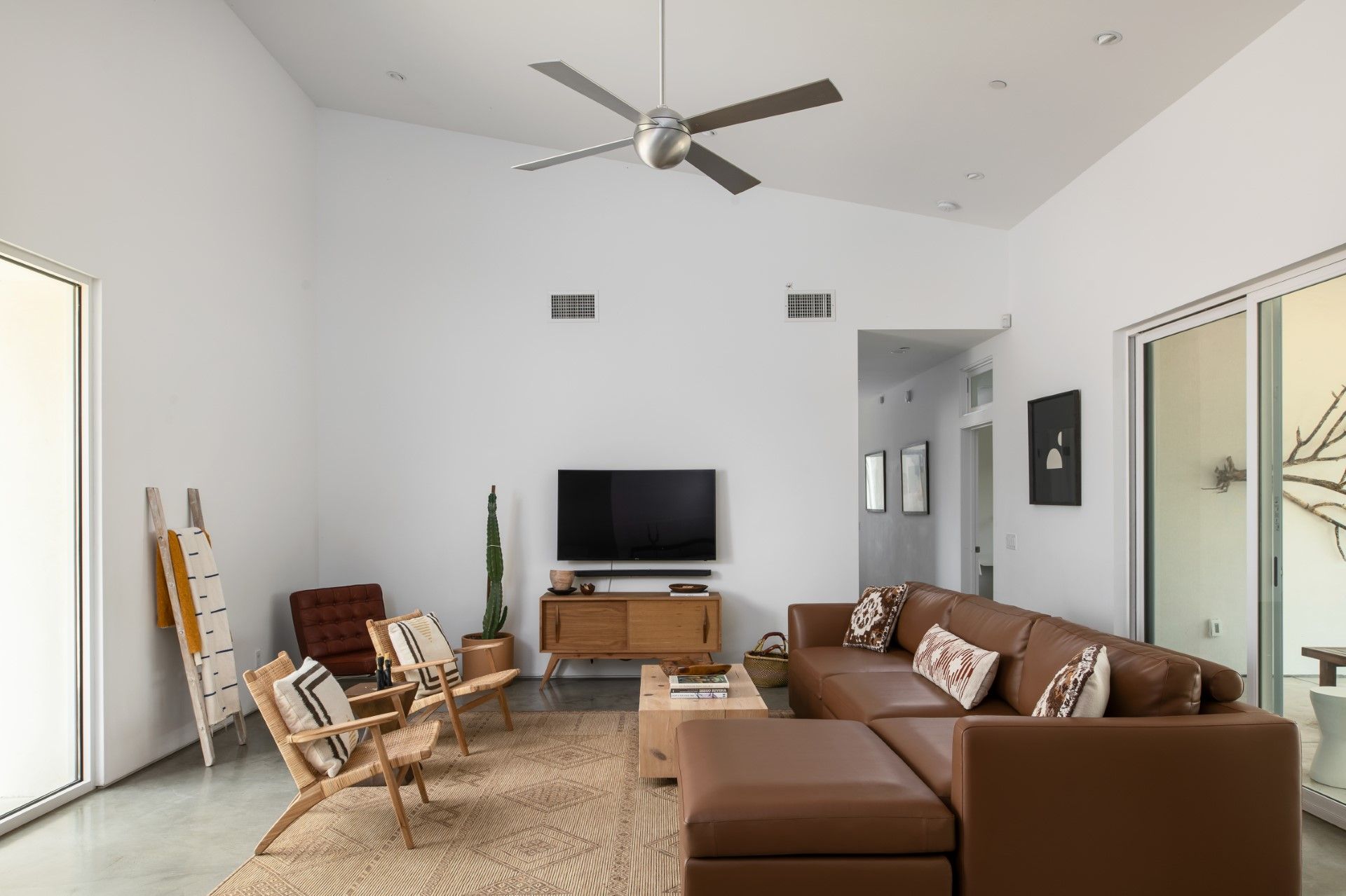 Spacious living room with vaulted ceiling, leather sectional, wooden furniture, and TV.