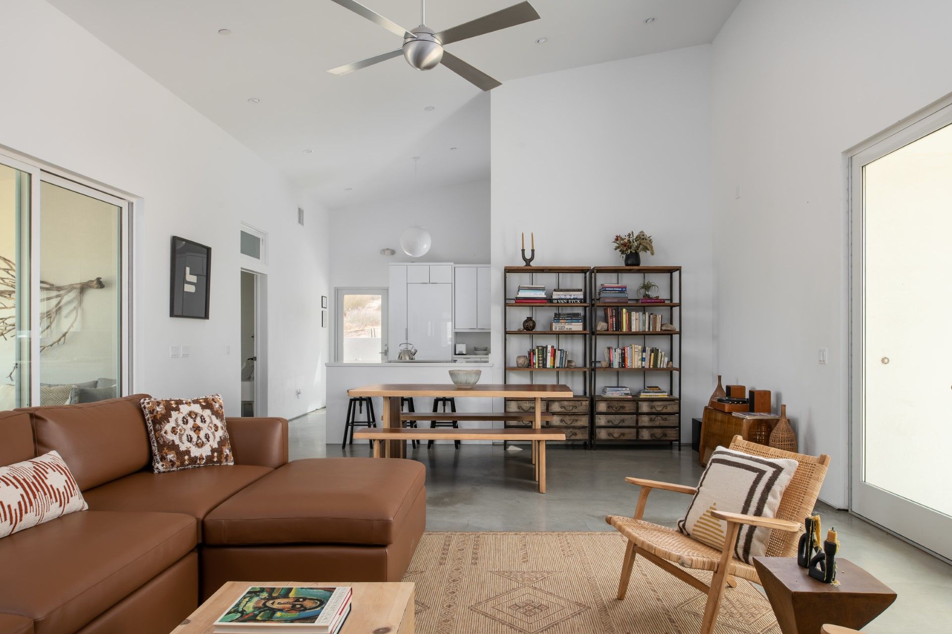Living room with leather sofa, dining table, bookshelf, and large windows.