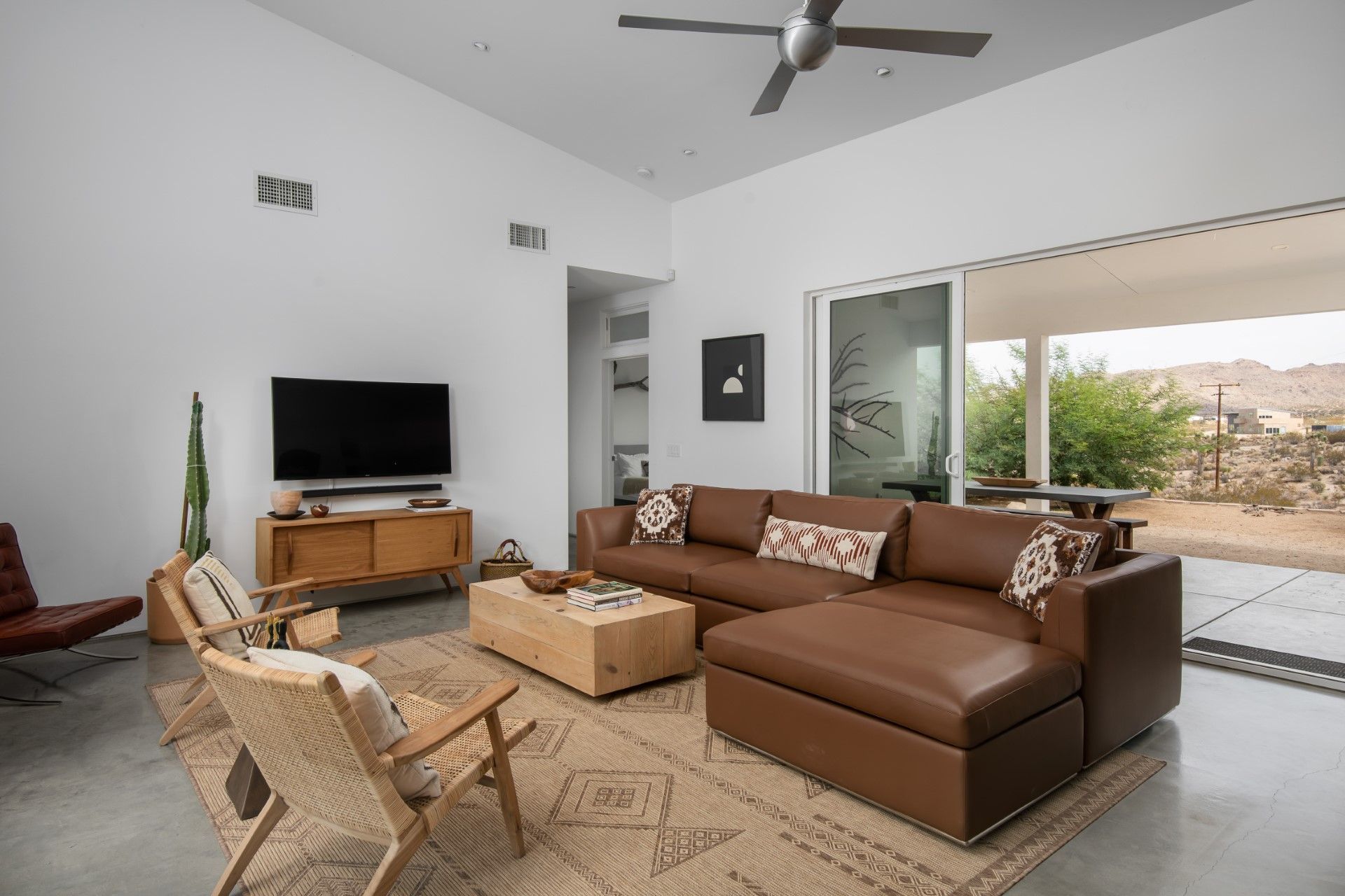 Modern living room with leather sectional, wood furniture, rug, TV, and outdoor access.
