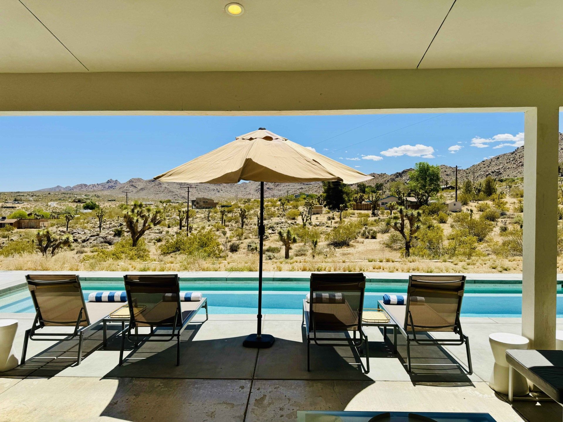 Poolside view with lounge chairs, umbrella, pool, and desert landscape in the background.