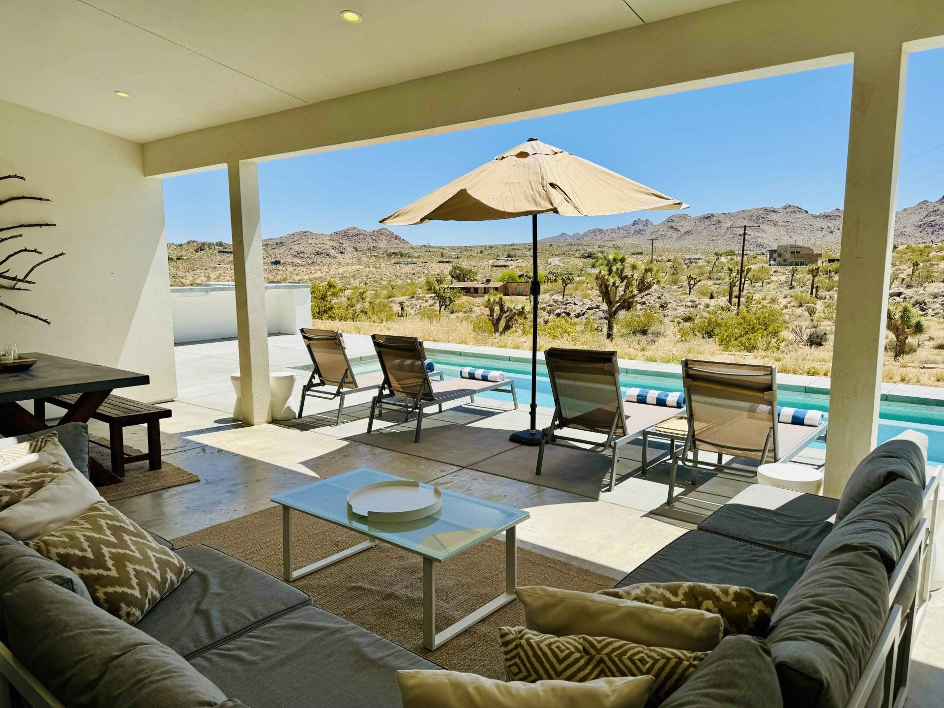 Patio with pool overlooking desert landscape. Lounge seating, umbrella, and sun chairs.