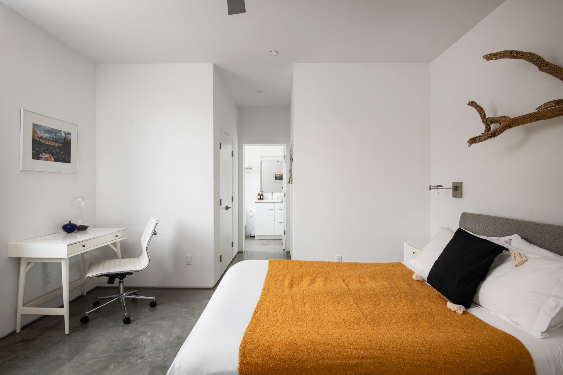 Bedroom with white walls, desk, bed with orange blanket, and a decorative branch.