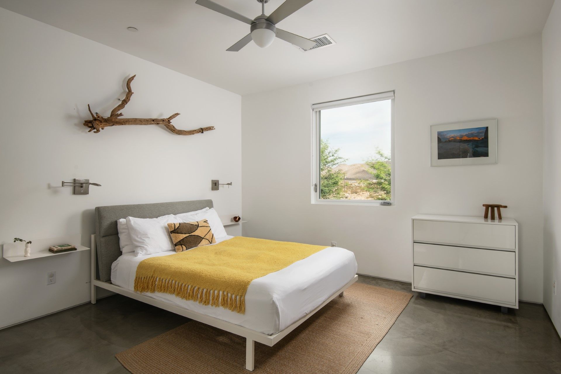 Bedroom with white walls, bed, window, dresser, and decorative driftwood.