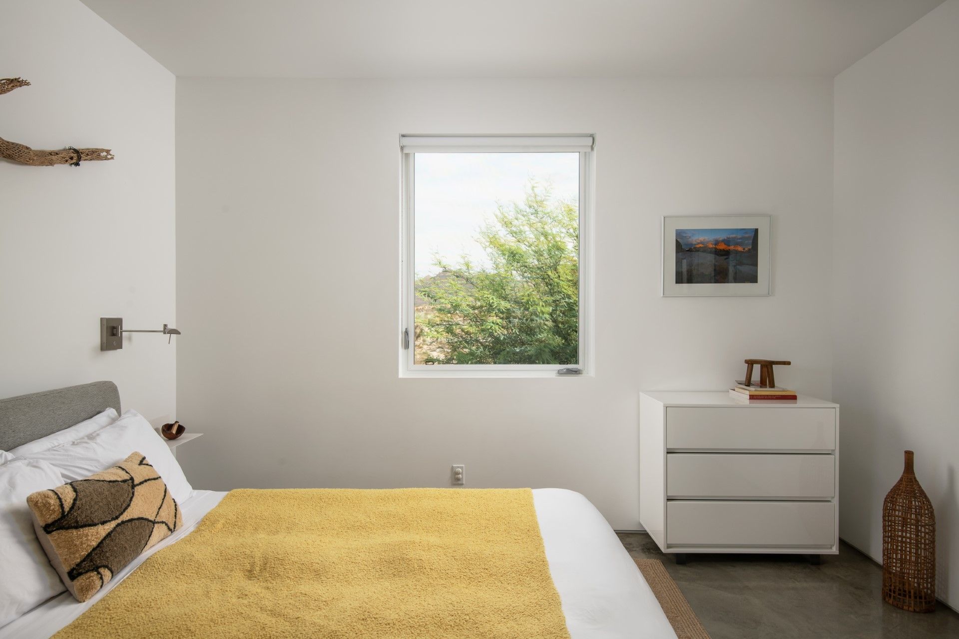 Bedroom with a white dresser, bed with yellow blanket, and a window with a view of greenery.