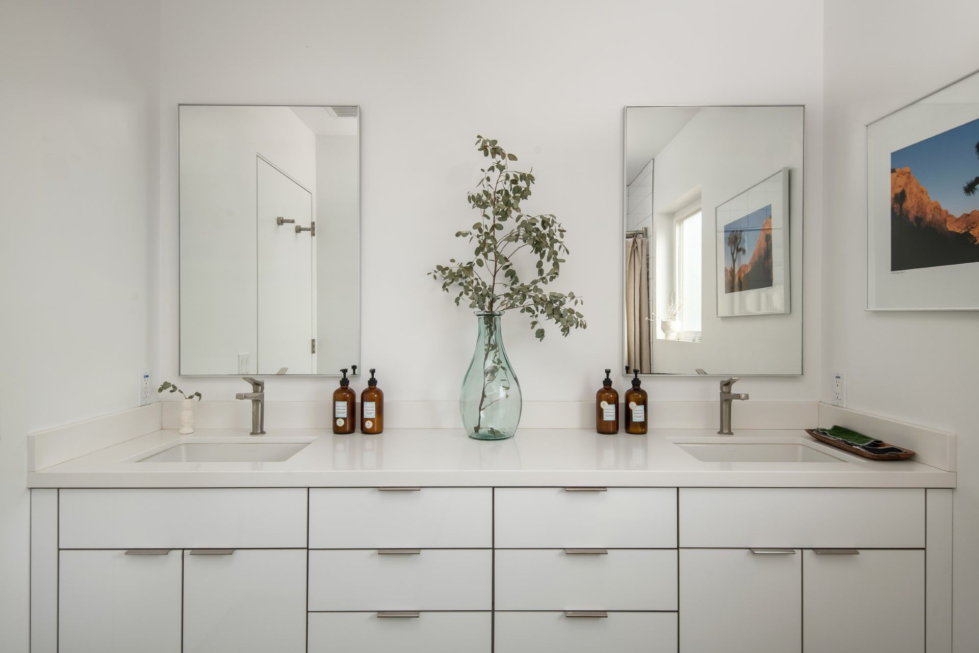 White bathroom vanity with two sinks, mirrors, and a decorative vase.