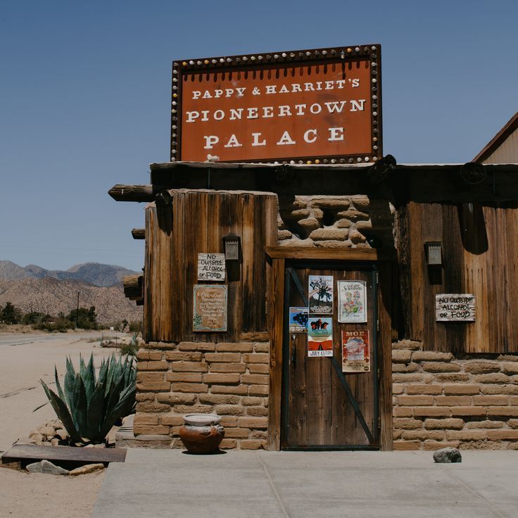Snowboarder in gray hoodie and goggles, smiles while fastening snowboard boot in snowy mountain setting.