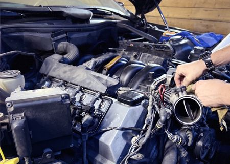 Hands working on car engine in a garage; close-up view of mechanical parts, tools visible.