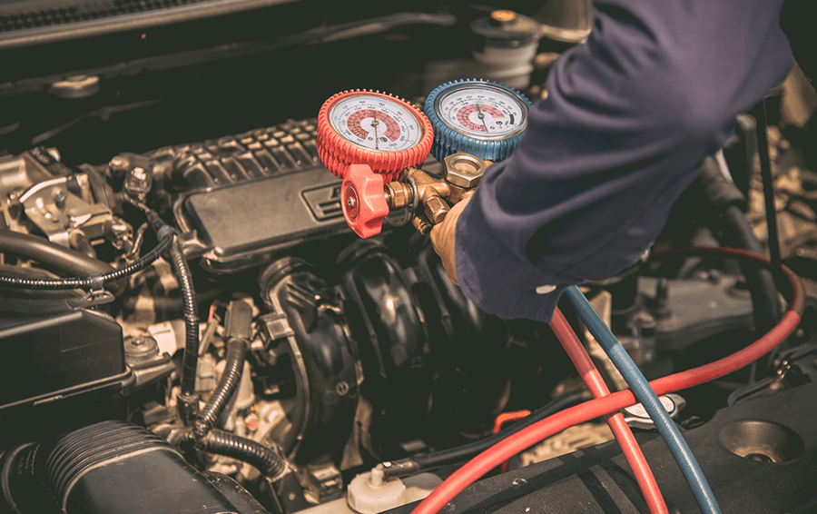 Mechanic attaching gauges to a car engine to test the air conditioning system.