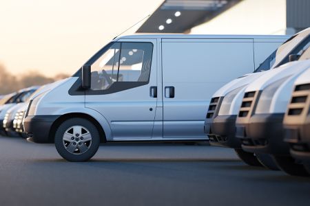 Line of silver cargo vans parked outdoors.