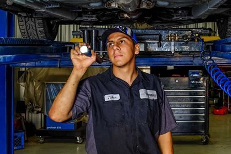 Mechanic working on a car's brakes in a shop. The car is red. The mechanic is using a wrench.
