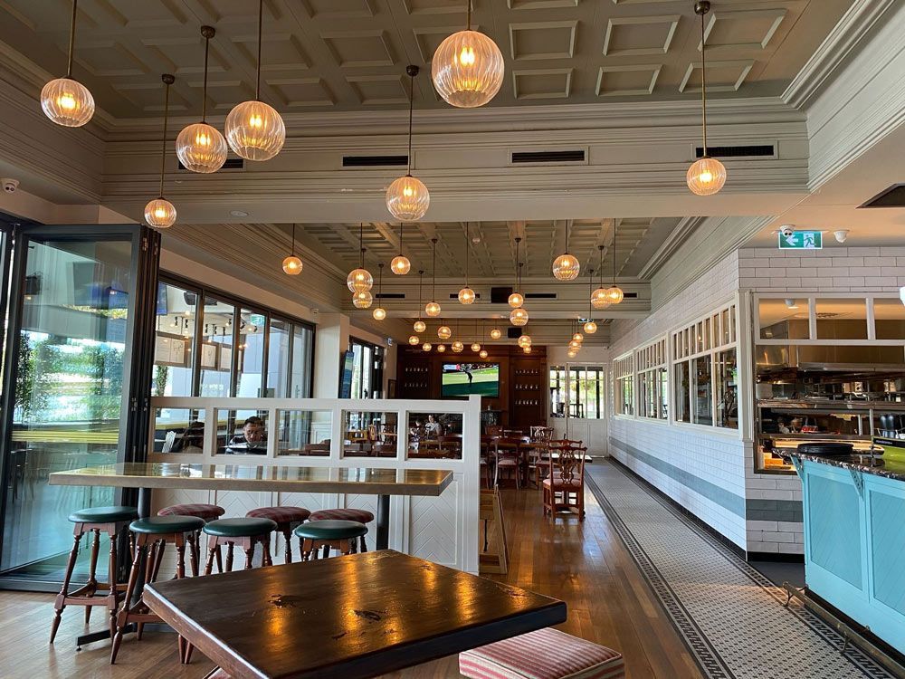 The inside of a restaurant with tables and stools and a bar.
