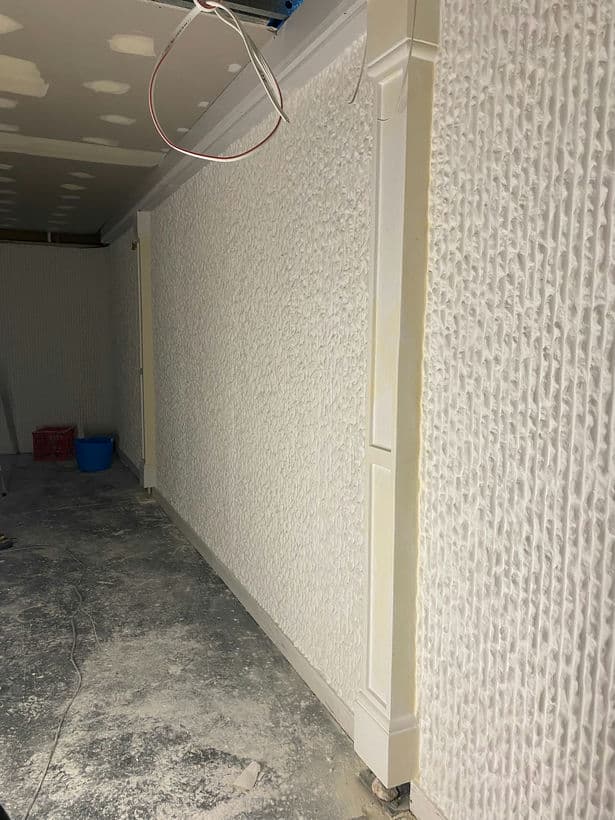 A long hallway with a white wall and a blue bucket on the floor.