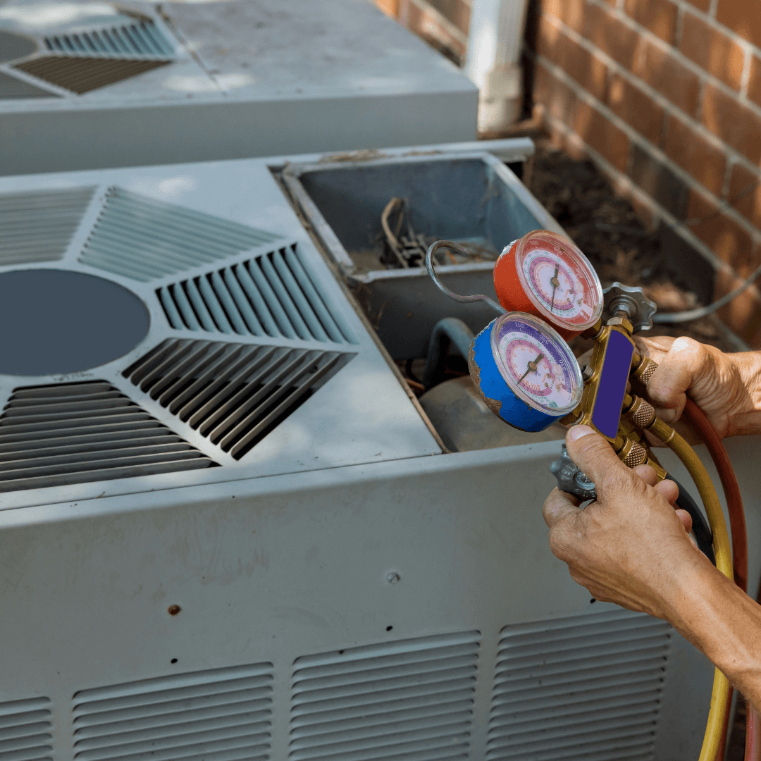A person is working on an air conditioner with gauges on it
