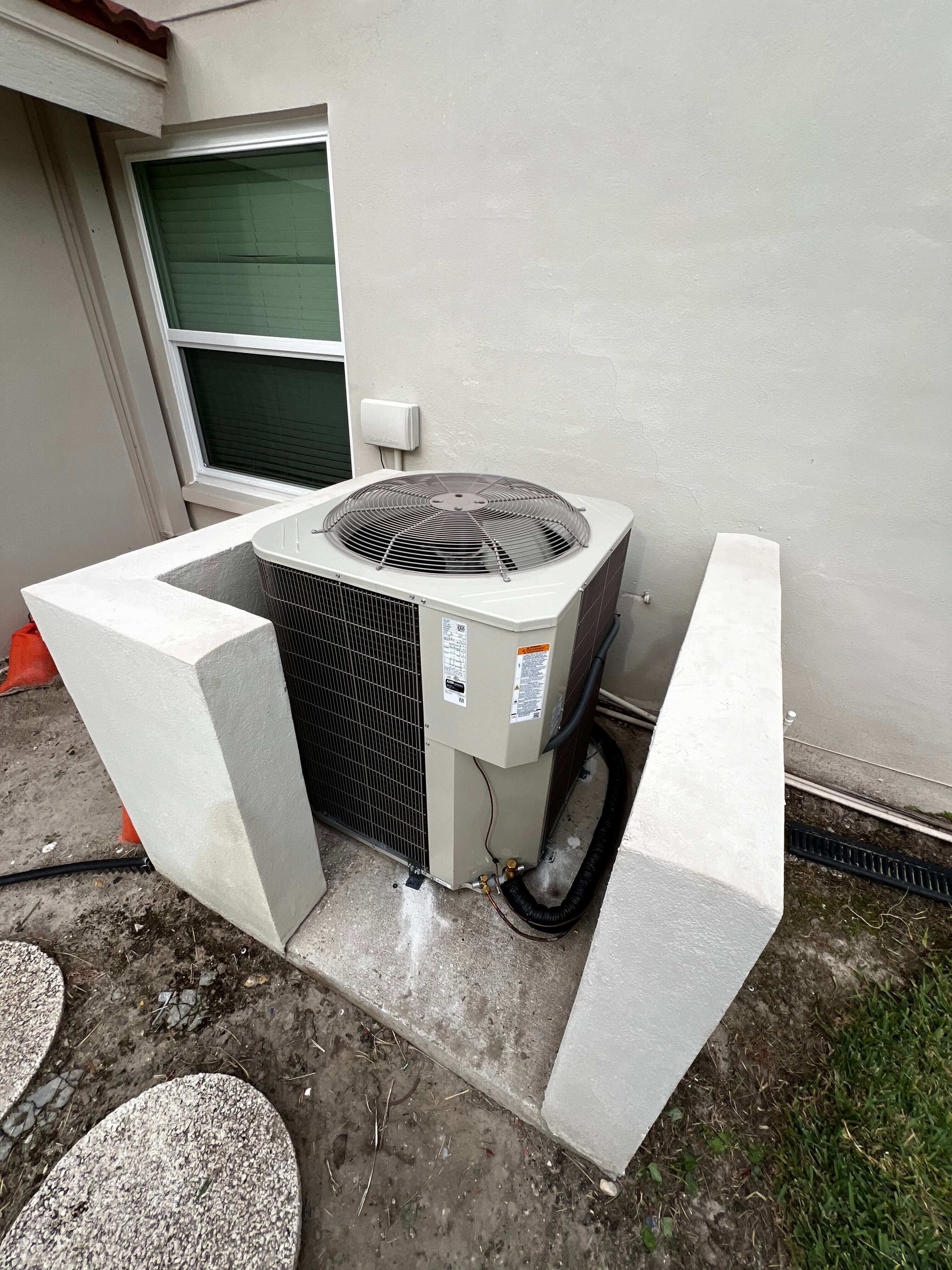 An air conditioner is sitting on top of a concrete block in front of a house.