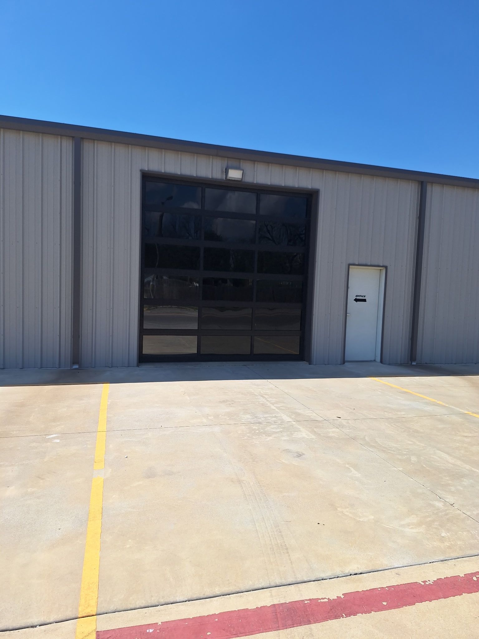 A tan metal industrial building exterior with a large glass sectional garage door and a single white entry door.
