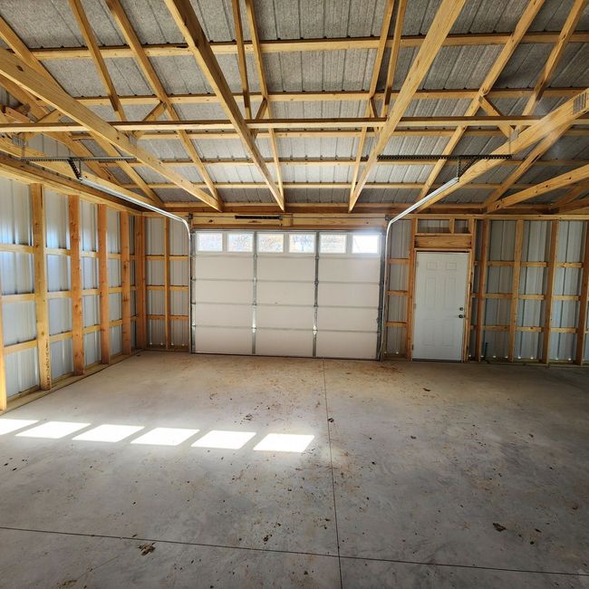 Interior of an unfinished pole barn with exposed wood framing, metal siding, a concrete floor, and a garage door.
