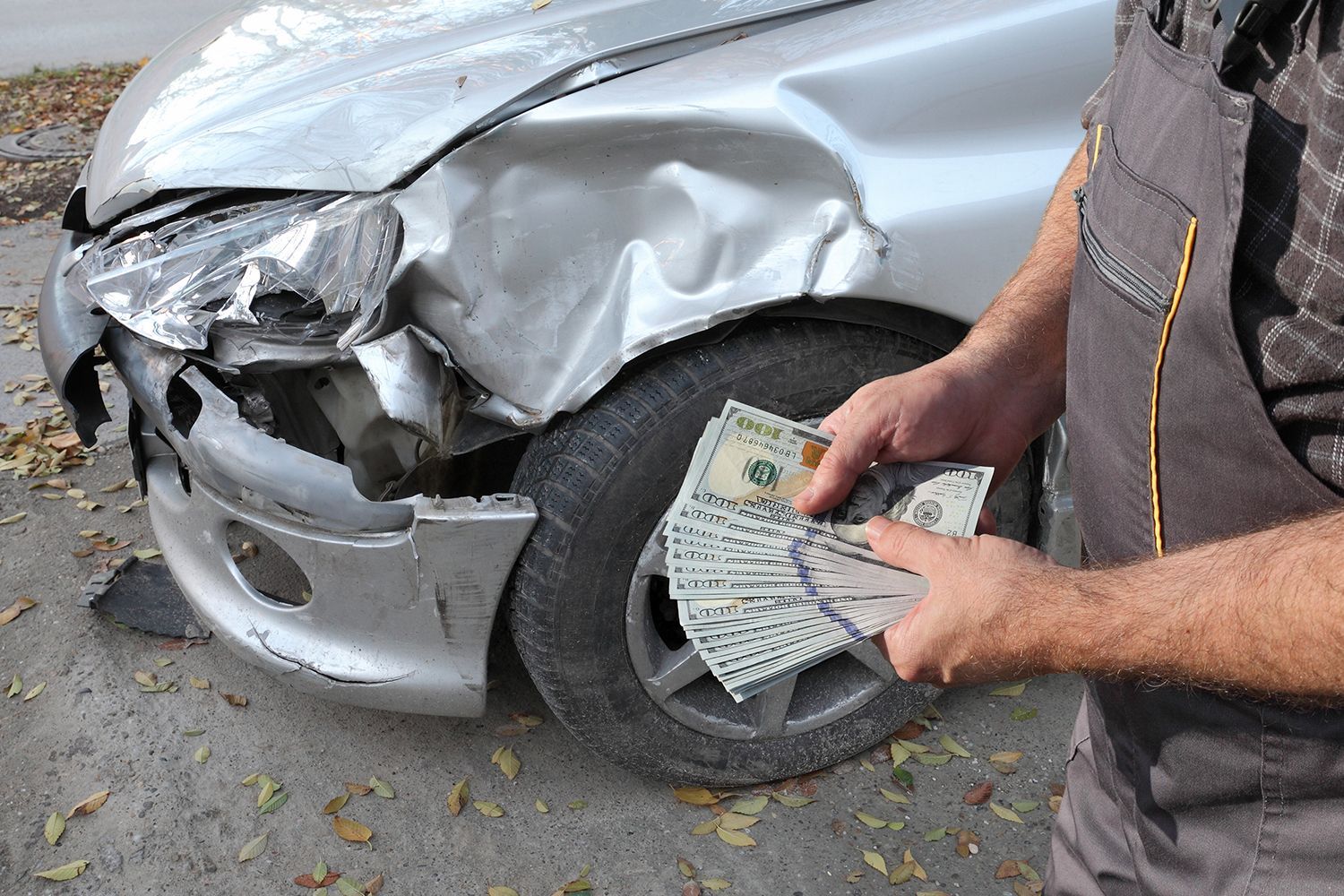 Damaged car inspection showcasing cash for junk cars with money held by mechanic hands.