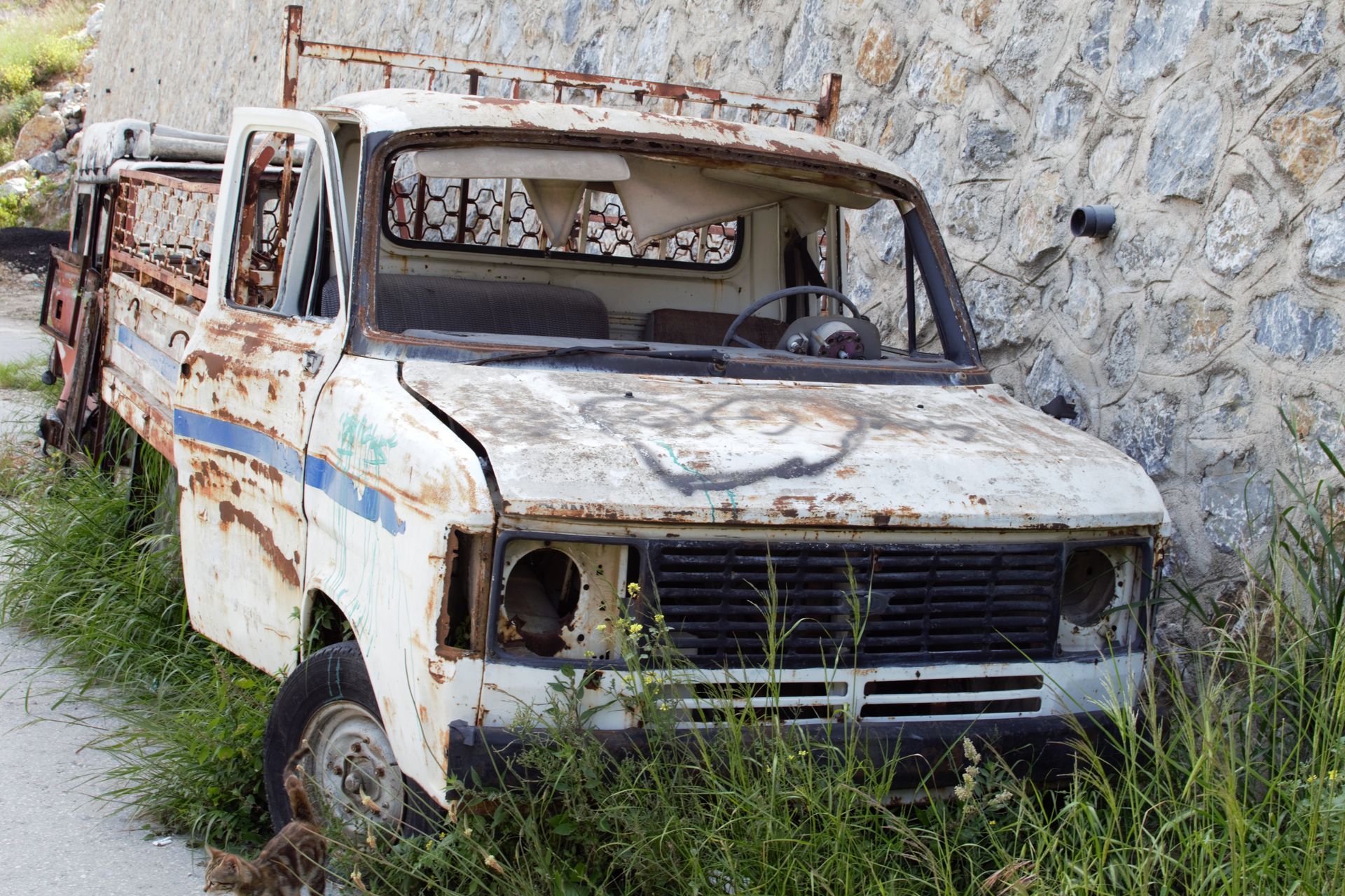 A junk car deteriorating outdoors with visible rust and damage.