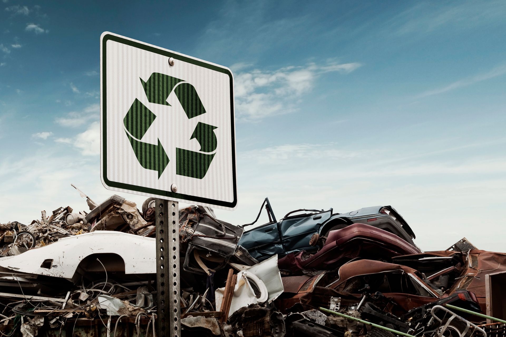 Recycling sign in front of a pile of crushed cars at a junkyard.