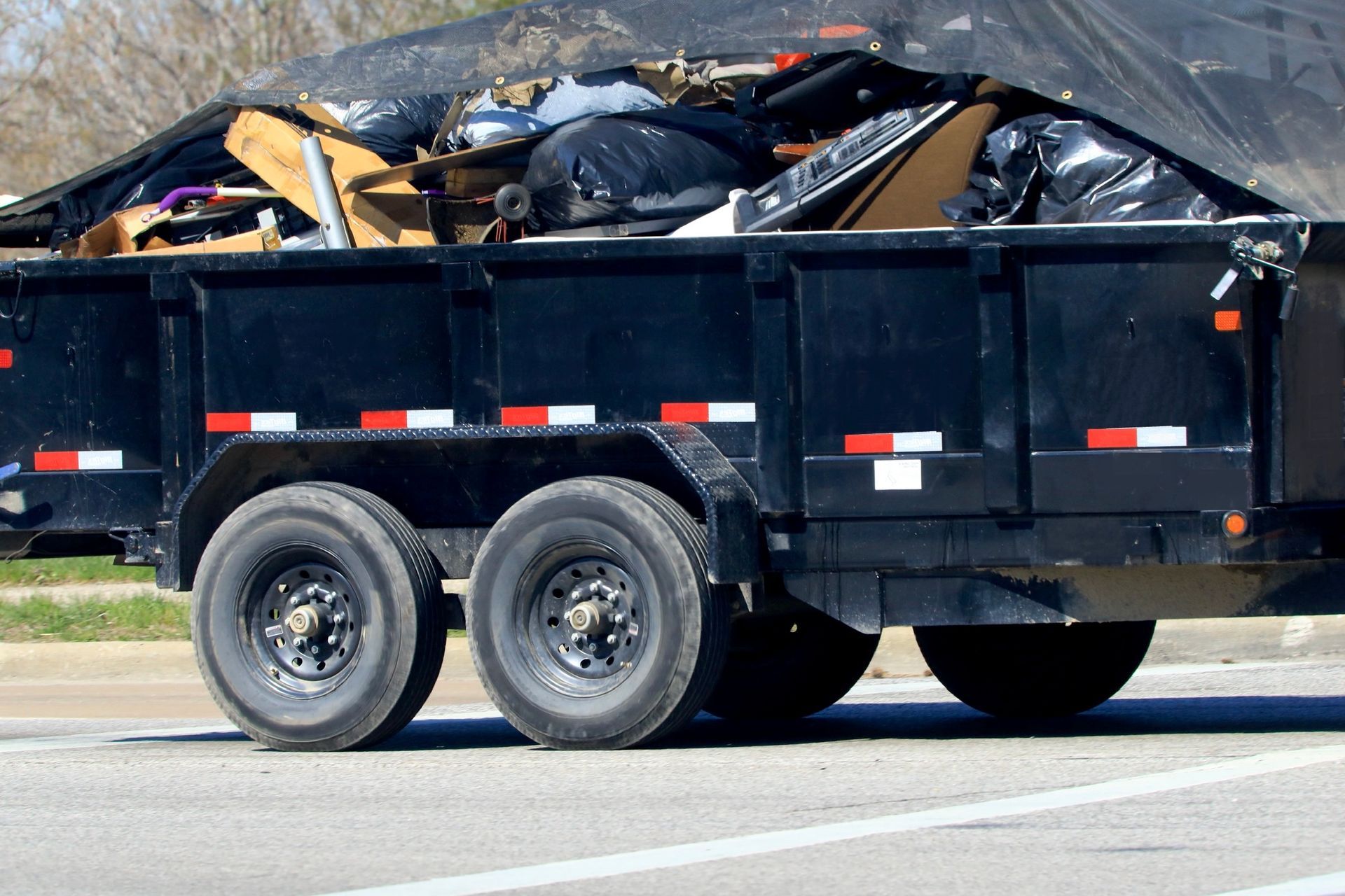 A black trailer filled with various items and trash bags.