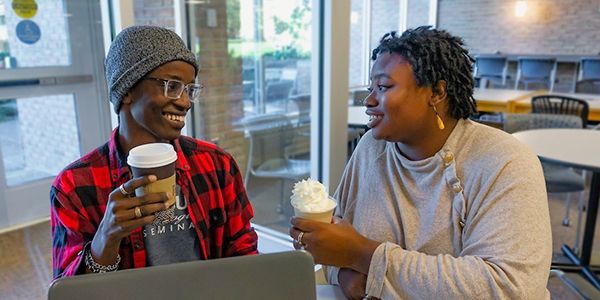 Two people smiling and talking while drinking coffee at a cafe.