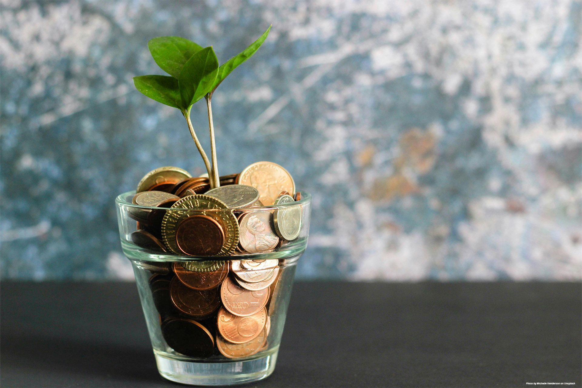 A small plant sprouts from coins inside a clear glass container, symbolizing financial savings.