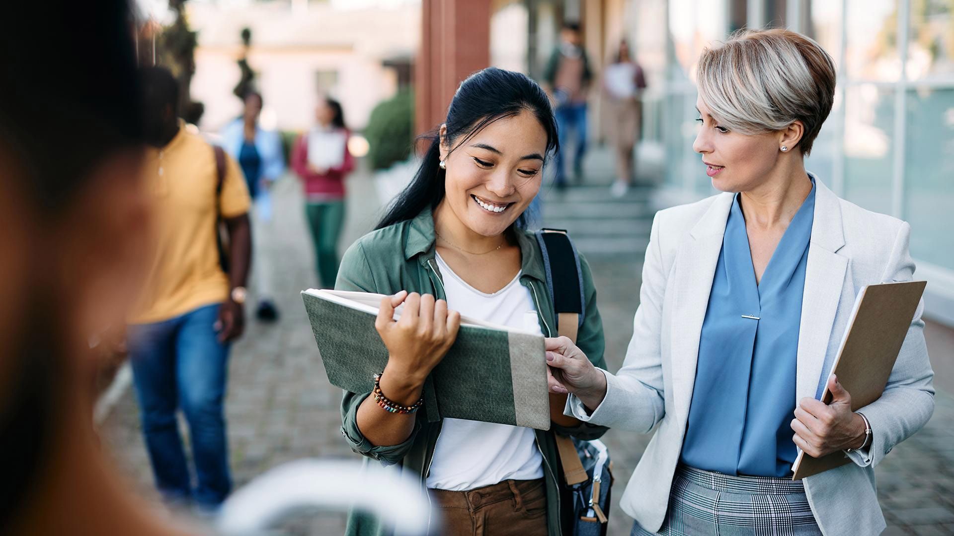 Two women are next to each other on campus looking at planning documents.