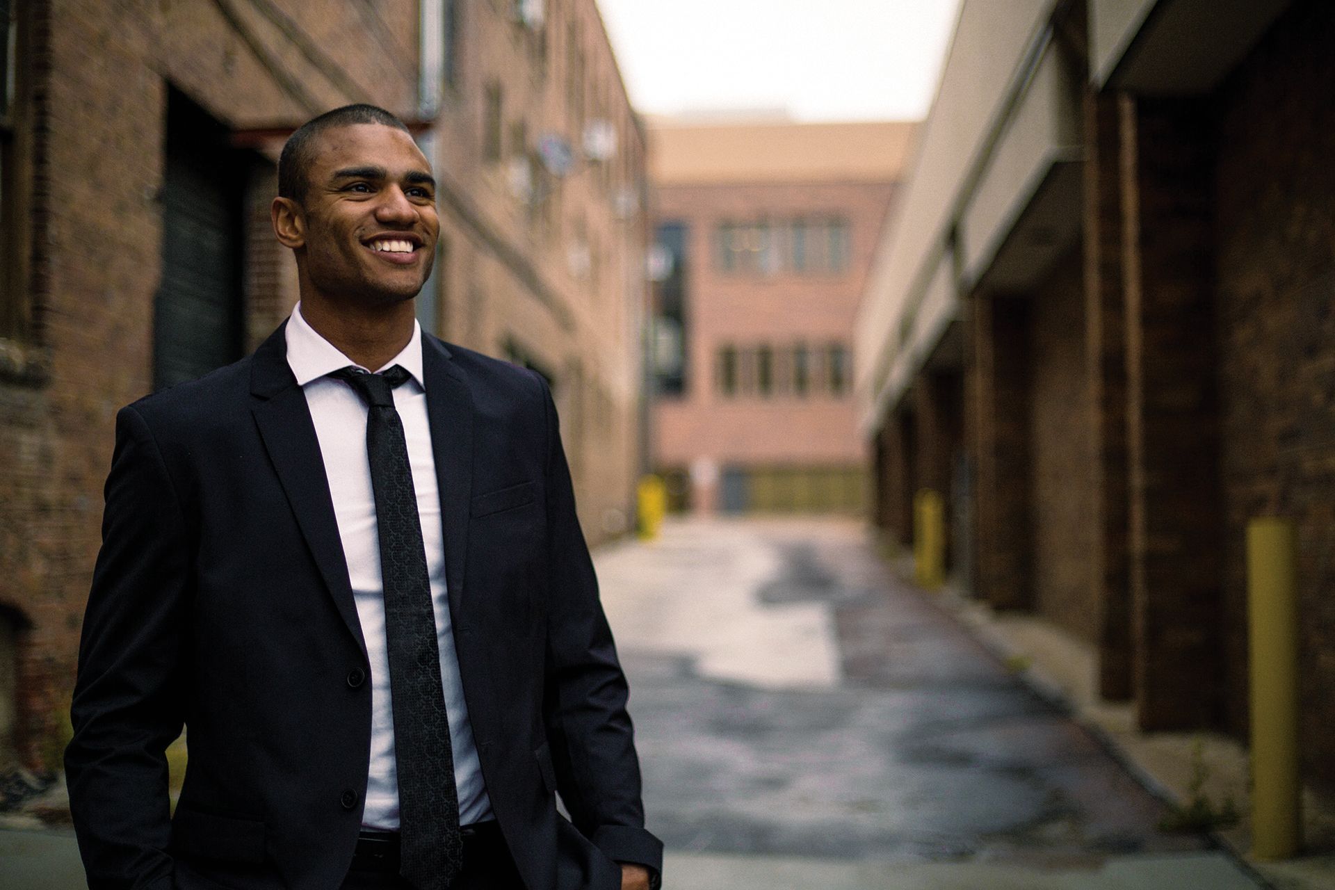 A man in a suit and tie is standing in an alleyway.