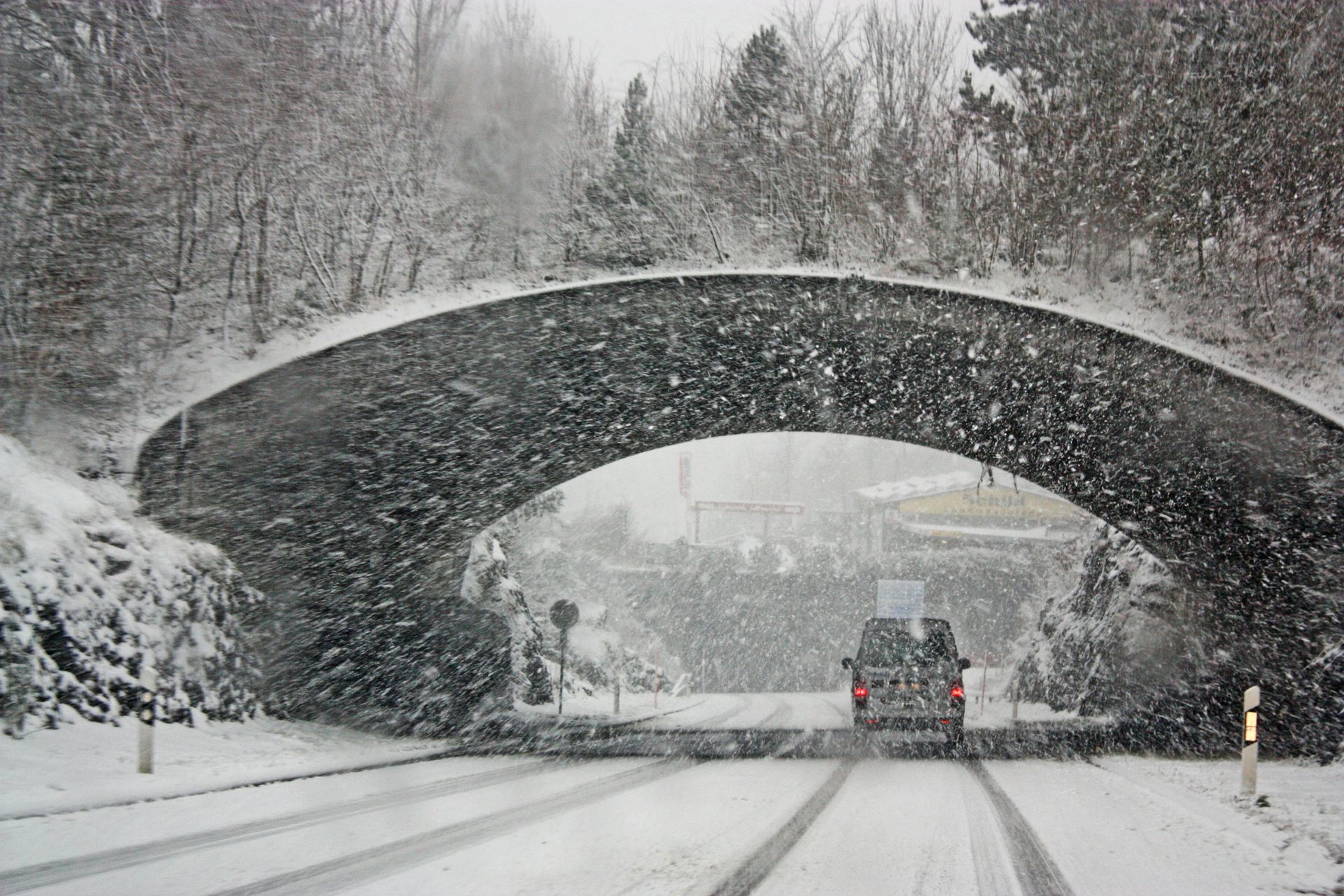 Snowy arched stone bridge over a campus road with a vehicle driving through.