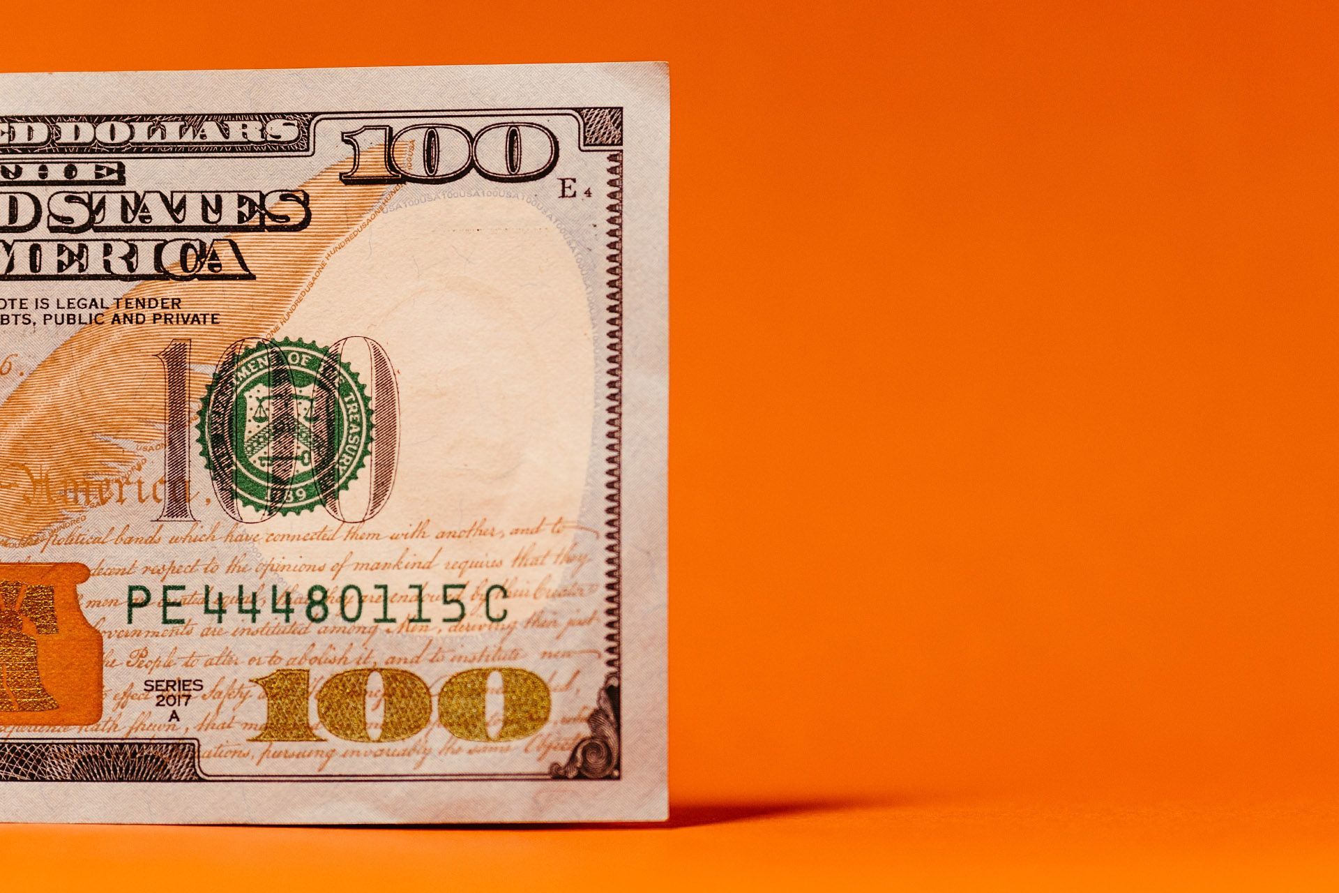 A close up of a 100 dollar bill on an orange background.