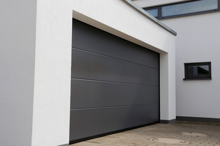 A gray garage door is on the side of a white building