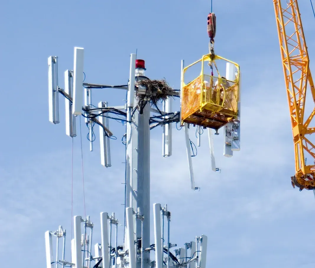 A crane is lifting a tower with antennas on it