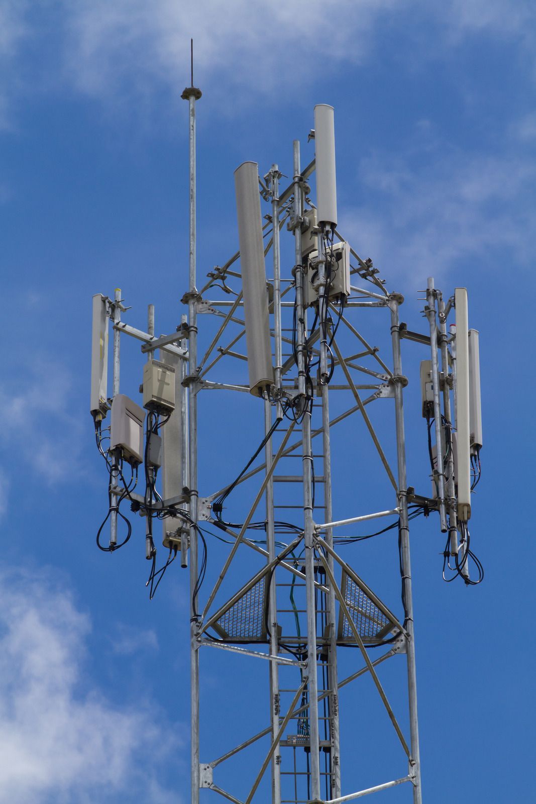 A telephone tower with many antennas against a blue sky