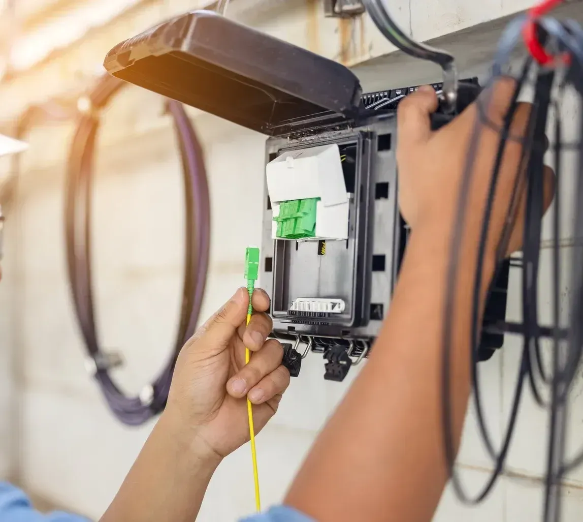 A man is working on a telephone box with a green cable coming out of it.