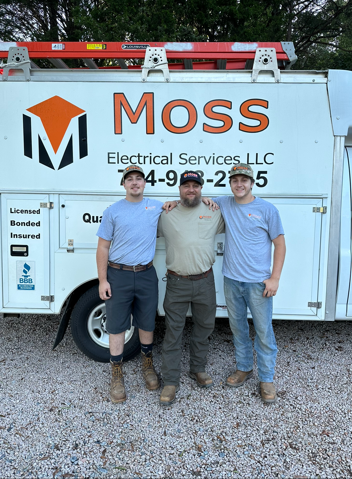 Three men are posing for a picture in front of a moss electrical services truck.